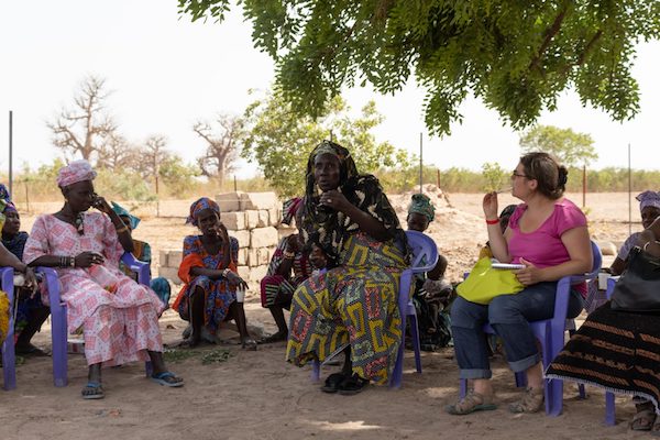 Group of women with colourful clothes sat under tree on plastic chairs